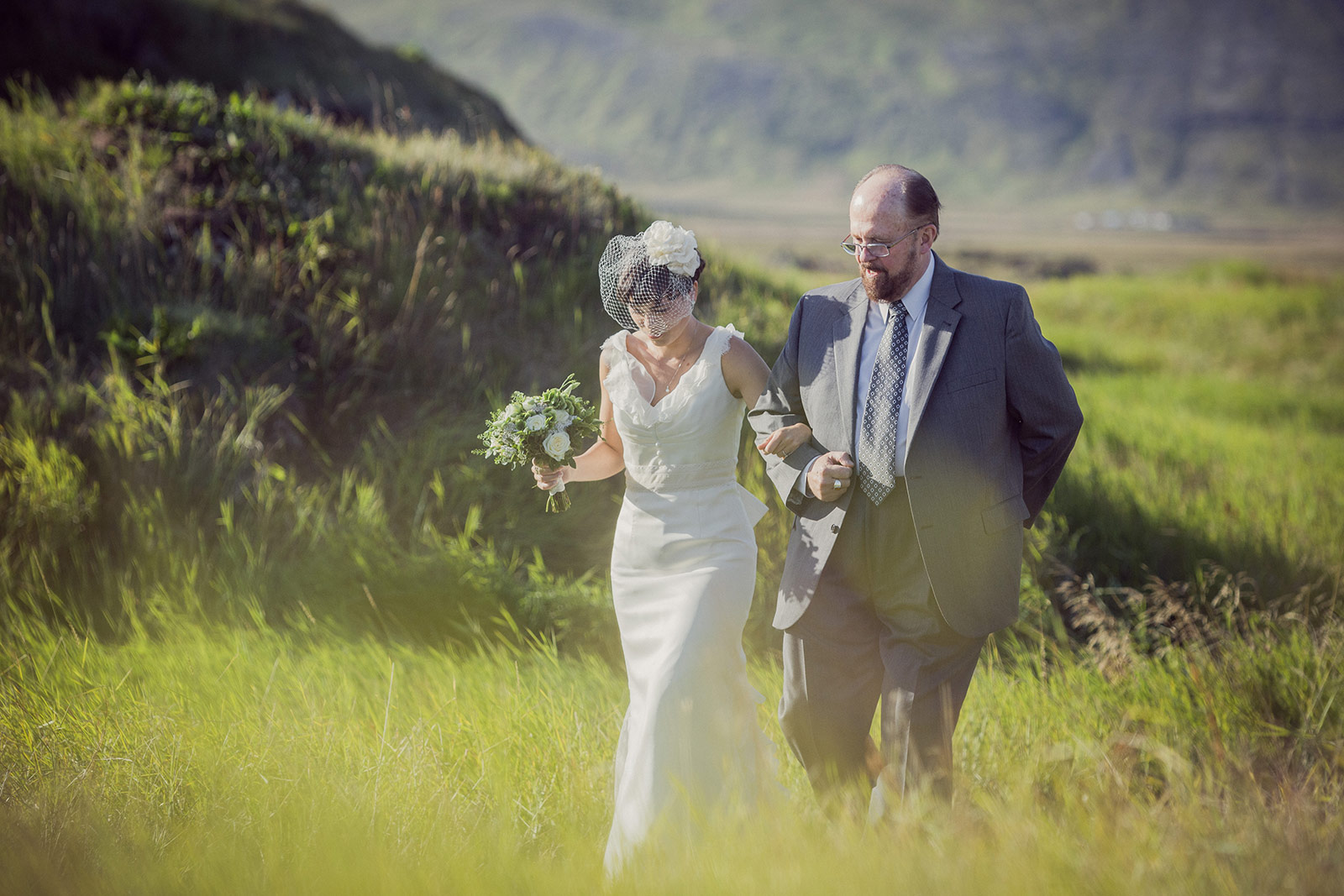 A bride and groom walking through the grass.