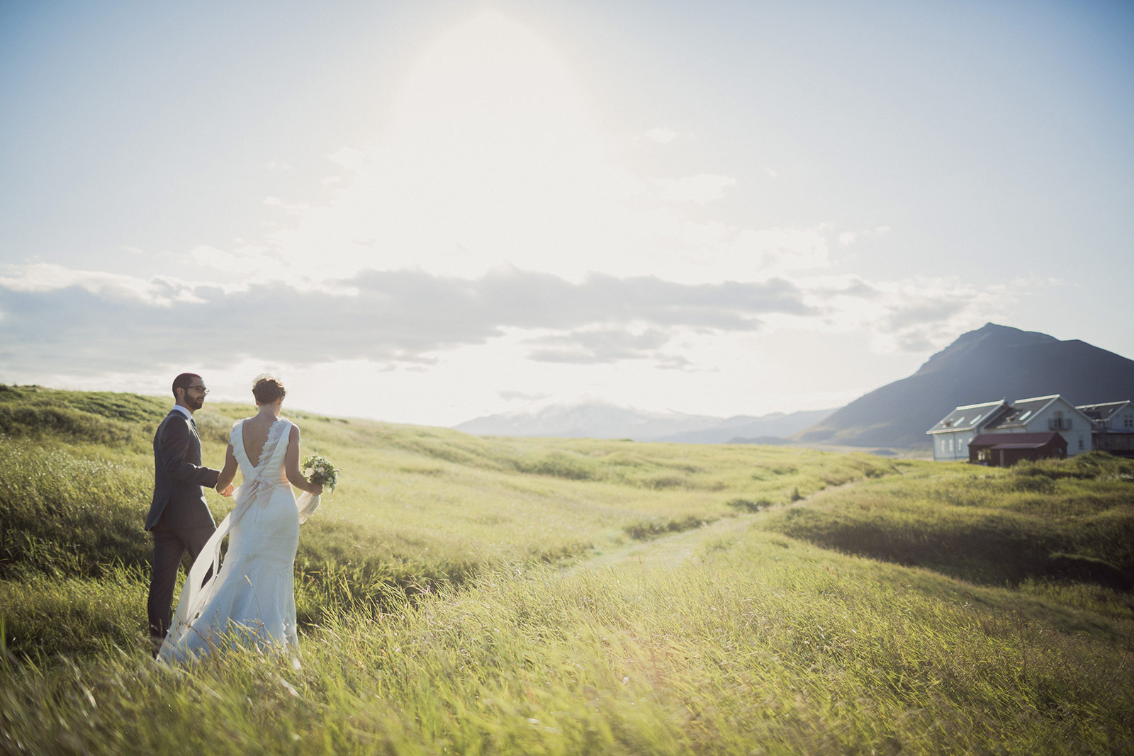 A bride and groom walking through the grass.