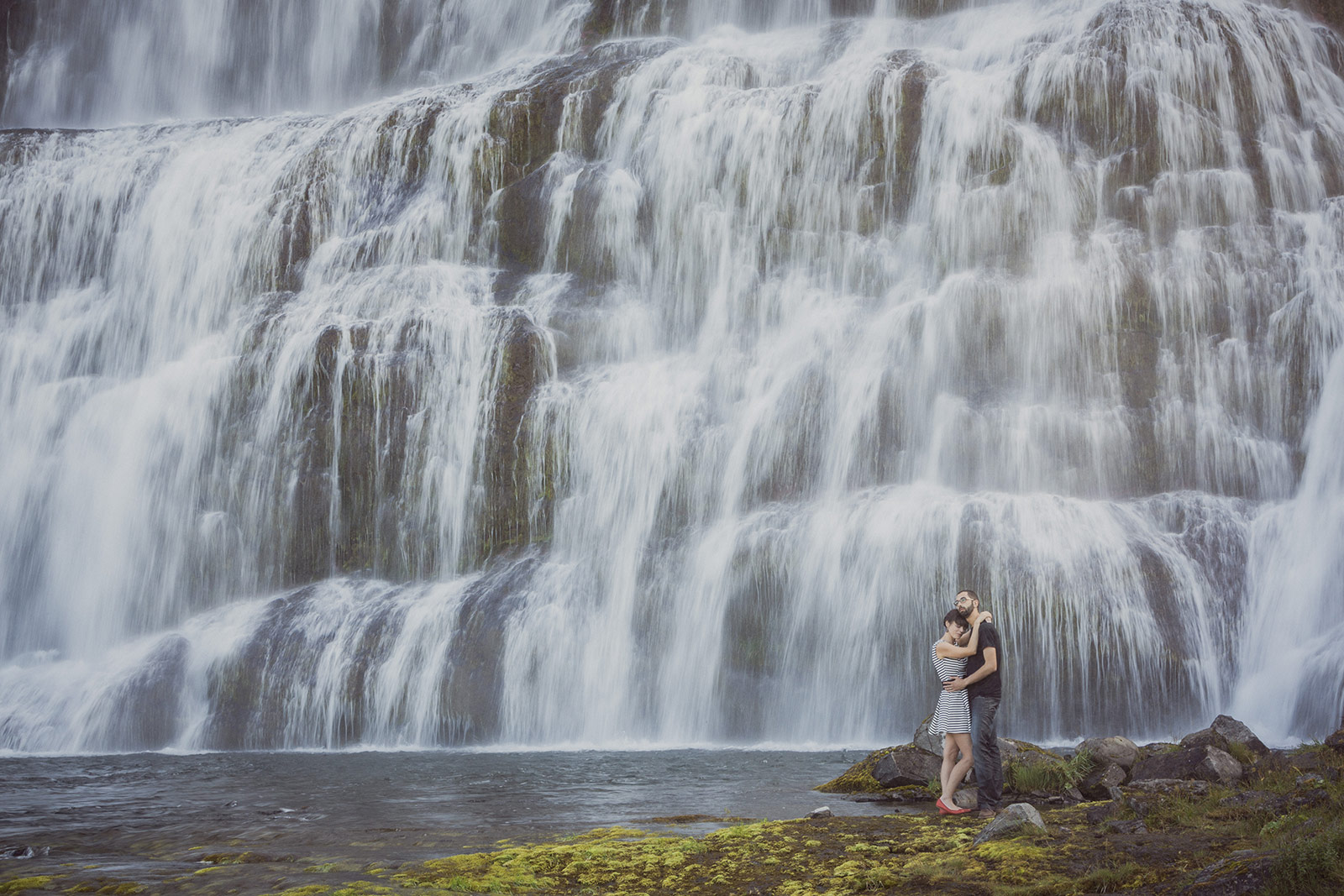 A man and woman standing in front of a waterfall.