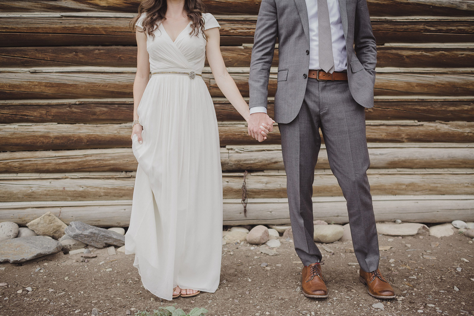 A man and woman holding hands in front of a log wall.