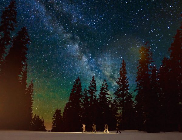 Three people standing in the snow under a night sky.