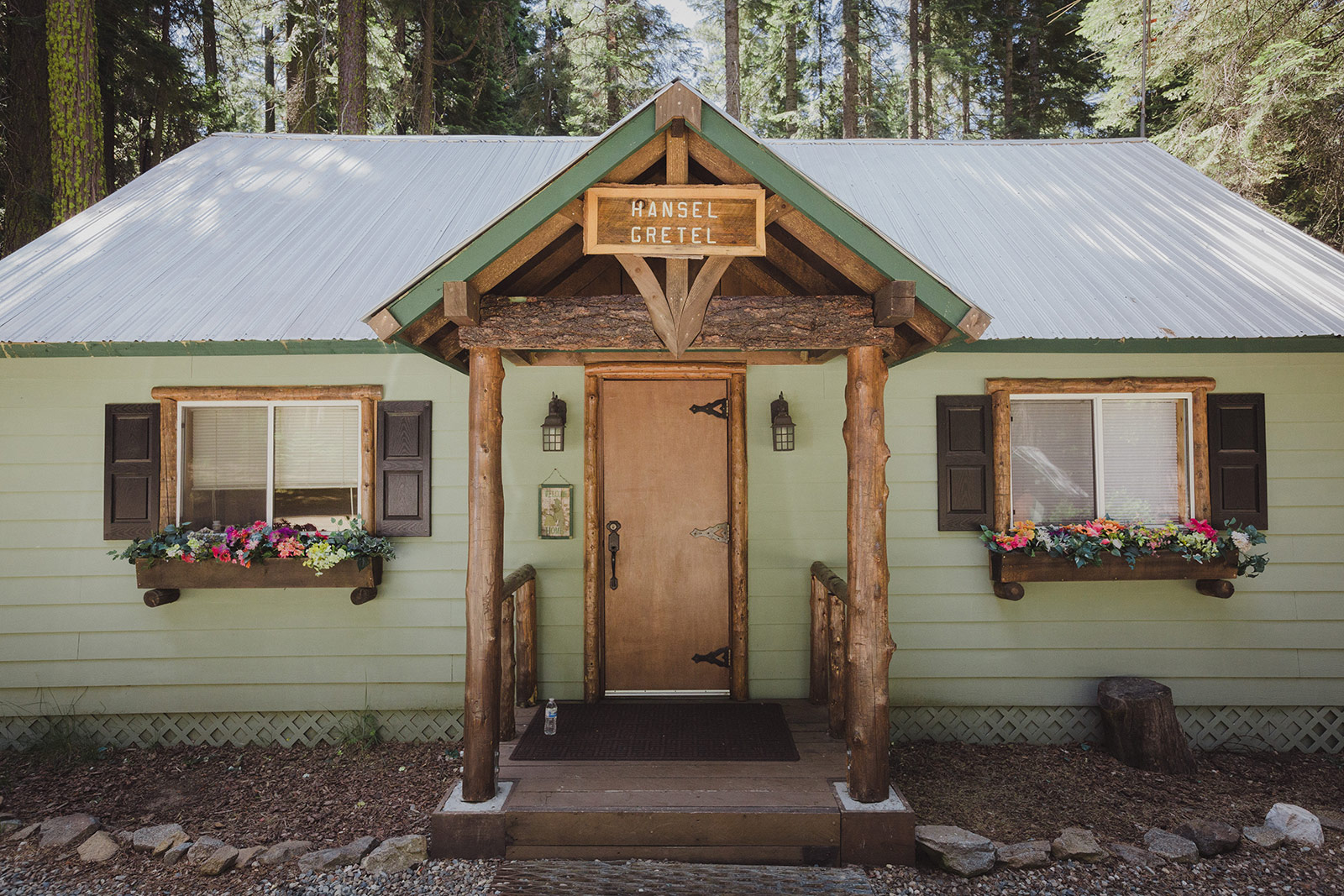 A green cabin with wooden steps and flowers on the porch.