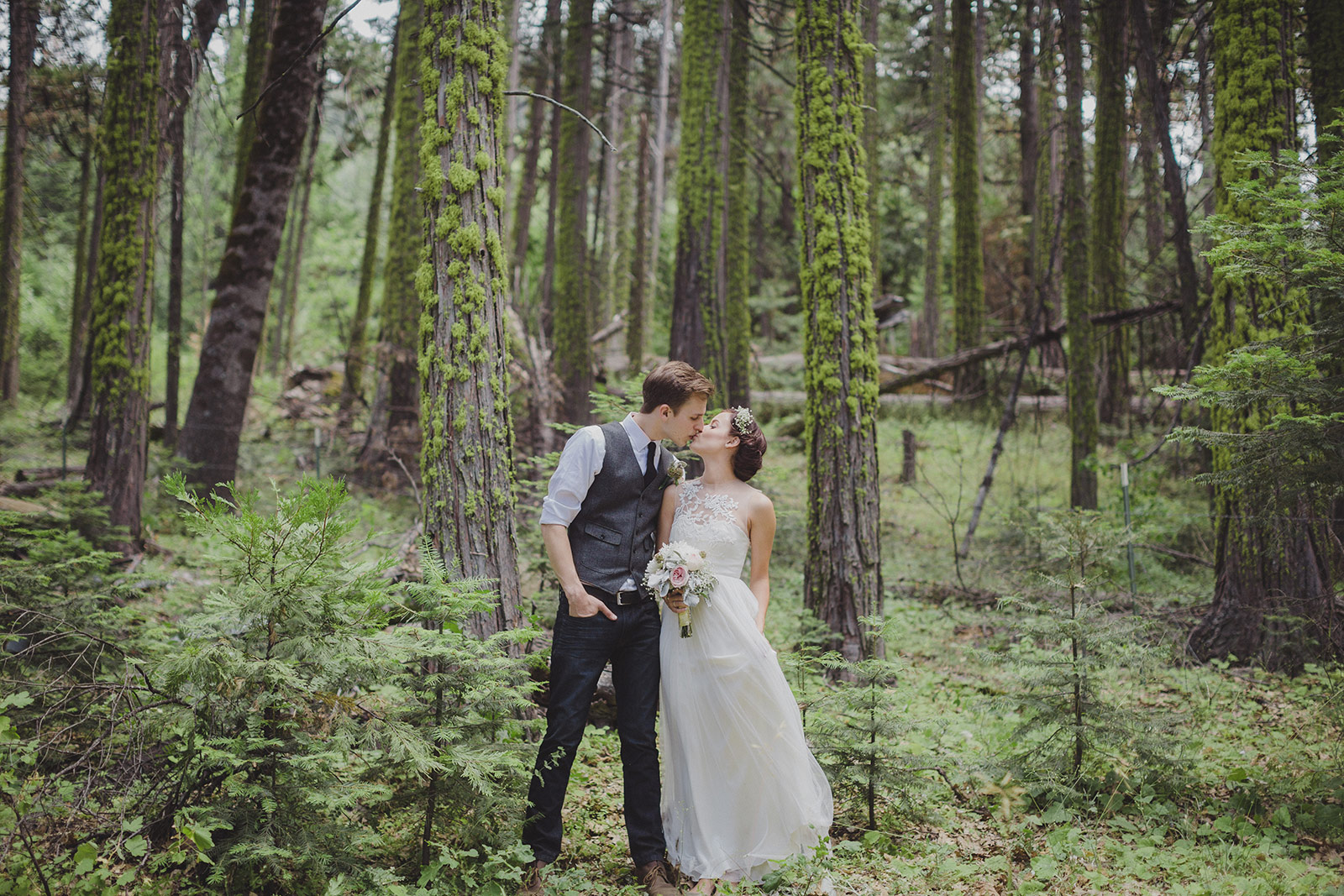 A man and woman kissing in the woods.