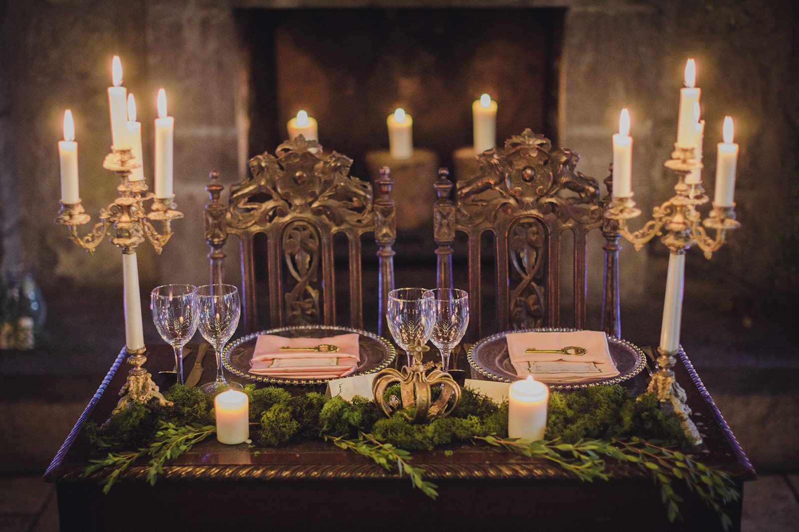 A table set with candles and plates in front of a fireplace.