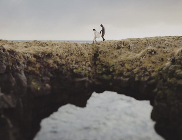 Two people walking on a cliff with water in the background.